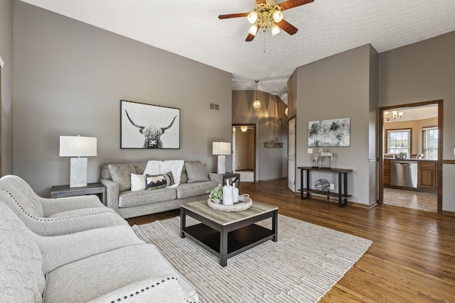 living room with ceiling fan, visible vents, vaulted ceiling, wood finished floors, and baseboards