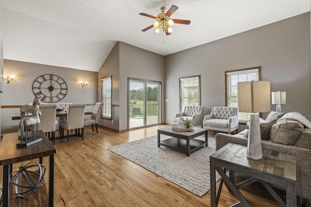 living area featuring a textured ceiling, ceiling fan, light wood-style flooring, and lofted ceiling