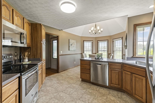 kitchen with brown cabinetry, appliances with stainless steel finishes, baseboards, a peninsula, and an inviting chandelier