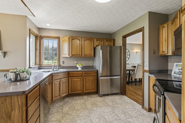 kitchen featuring brown cabinets, dark countertops, a sink, a textured ceiling, and stainless steel appliances