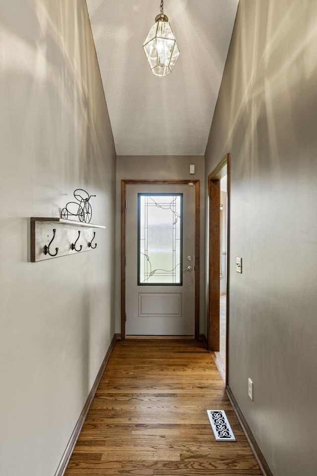 entryway featuring baseboards, visible vents, wood finished floors, and lofted ceiling