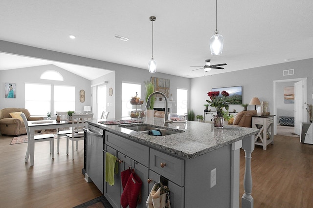 kitchen with wood finished floors, a center island with sink, a sink, stainless steel dishwasher, and open floor plan