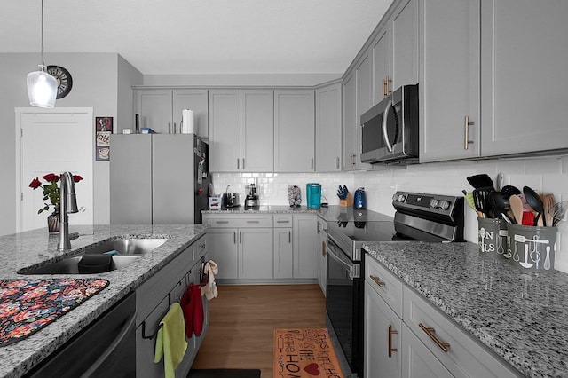 kitchen with tasteful backsplash, light wood finished floors, pendant lighting, stainless steel appliances, and a sink