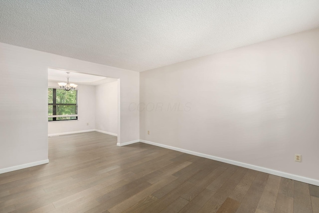 unfurnished room with an inviting chandelier, dark wood-type flooring, and baseboards