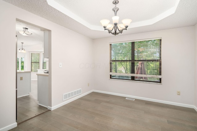 unfurnished room with an inviting chandelier, a raised ceiling, wood finished floors, and visible vents