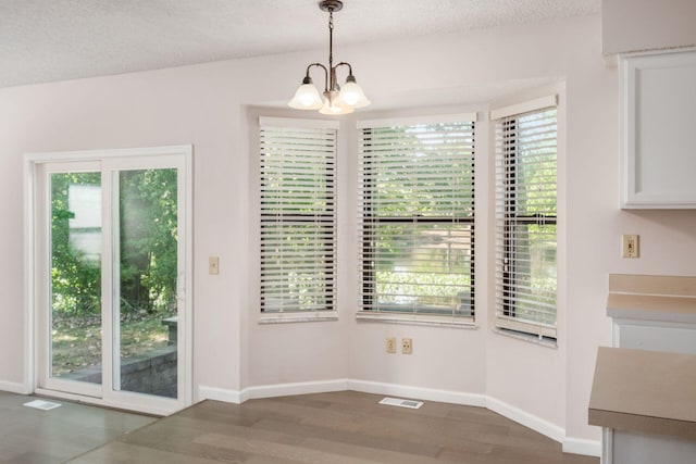 unfurnished dining area featuring a textured ceiling, visible vents, a chandelier, baseboards, and wood finished floors