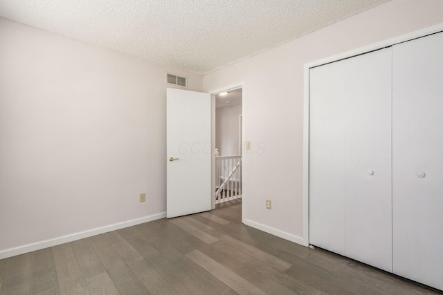 unfurnished bedroom featuring baseboards, a textured ceiling, visible vents, and wood finished floors