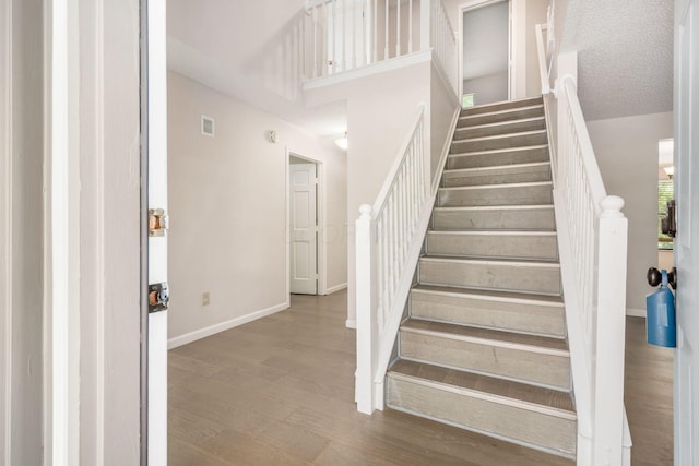 staircase featuring a textured ceiling, visible vents, baseboards, wood finished floors, and a high ceiling