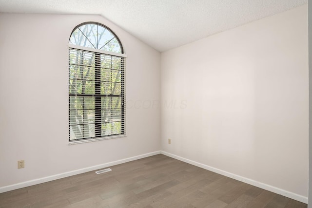 empty room featuring a textured ceiling, visible vents, baseboards, wood finished floors, and lofted ceiling