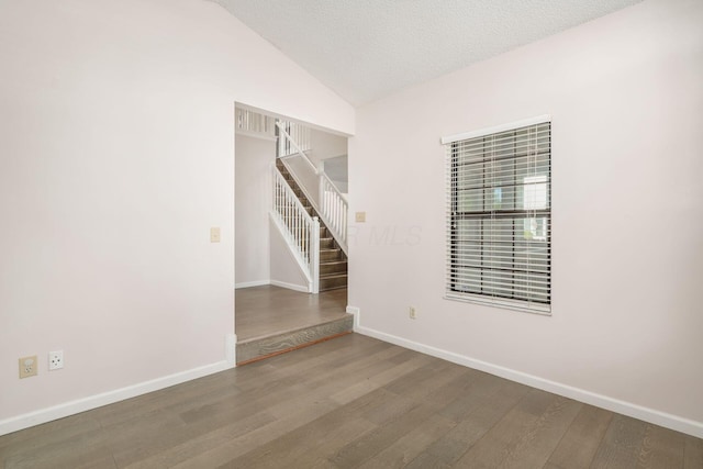 unfurnished room featuring baseboards, lofted ceiling, stairway, and wood finished floors