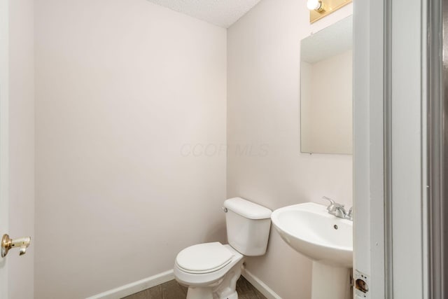 half bathroom featuring toilet, a sink, baseboards, and a textured ceiling