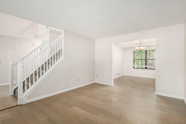 spare room featuring baseboards, wood finished floors, an inviting chandelier, and stairway