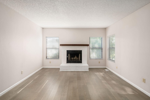 unfurnished living room featuring a textured ceiling, baseboards, wood finished floors, and a brick fireplace