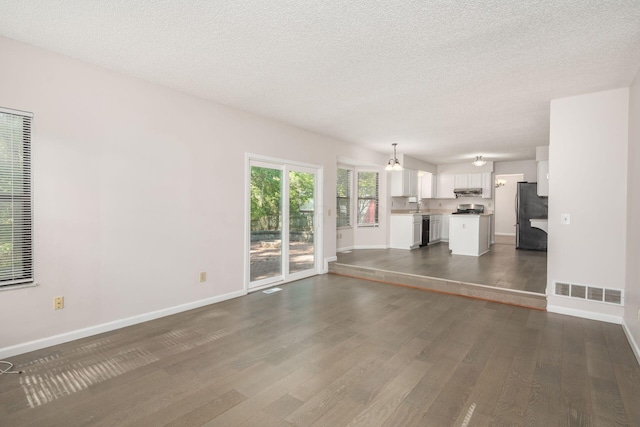 unfurnished living room featuring dark wood finished floors, baseboards, visible vents, and a textured ceiling