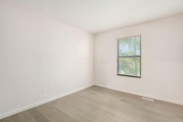 spare room with baseboards, a textured ceiling, light wood-style flooring, and visible vents