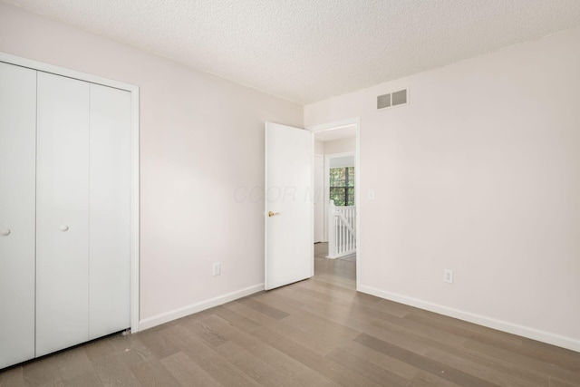 unfurnished bedroom with a closet, wood finished floors, a textured ceiling, baseboards, and visible vents