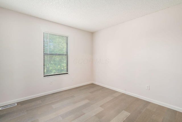 unfurnished room with baseboards, visible vents, wood finished floors, and a textured ceiling