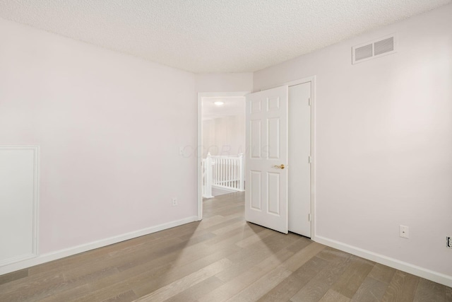 spare room featuring wood finished floors, a textured ceiling, baseboards, and visible vents