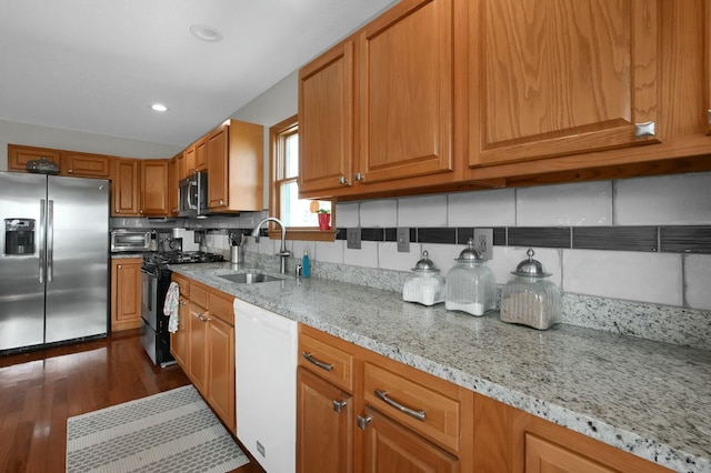 kitchen with a sink, backsplash, light stone countertops, appliances with stainless steel finishes, and brown cabinets