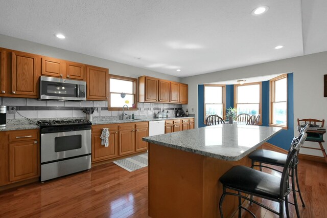 kitchen with light stone countertops, appliances with stainless steel finishes, a sink, dark wood-style floors, and a kitchen breakfast bar