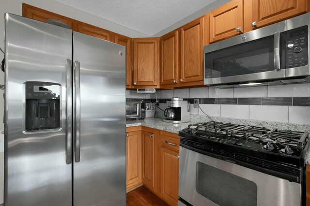 kitchen with tasteful backsplash, a textured ceiling, brown cabinets, stainless steel appliances, and dark wood-type flooring