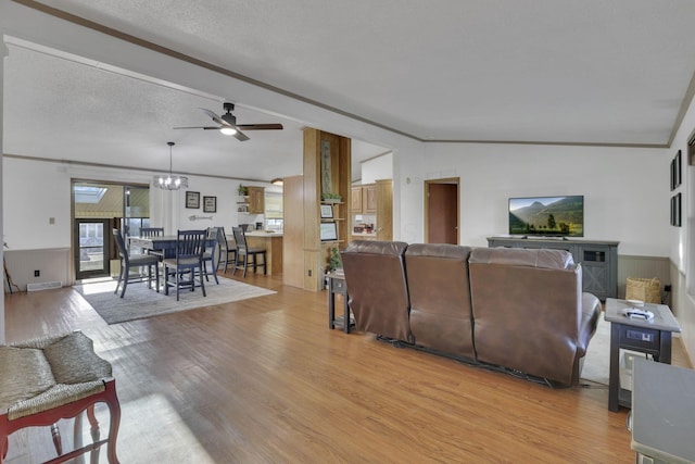 living area featuring light wood finished floors, ornamental molding, vaulted ceiling, ceiling fan with notable chandelier, and a textured ceiling