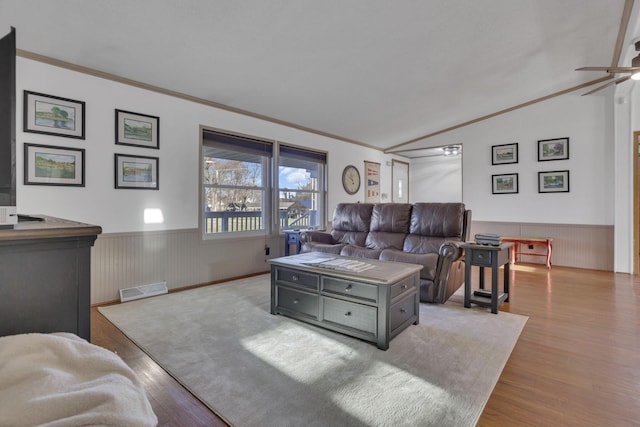 living area featuring lofted ceiling, wood finished floors, visible vents, and wainscoting