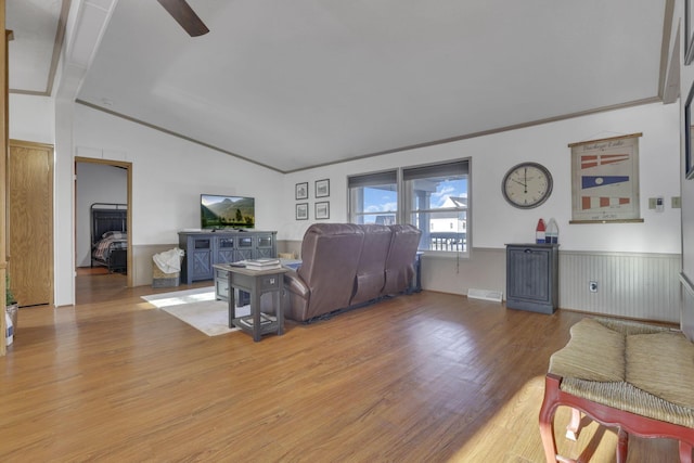 living area featuring light wood-style flooring, a ceiling fan, wainscoting, crown molding, and lofted ceiling