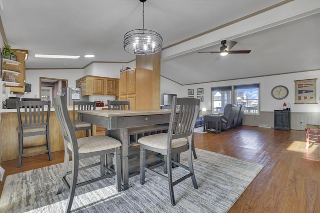 dining room featuring a wainscoted wall, lofted ceiling with beams, ornamental molding, ceiling fan with notable chandelier, and wood finished floors