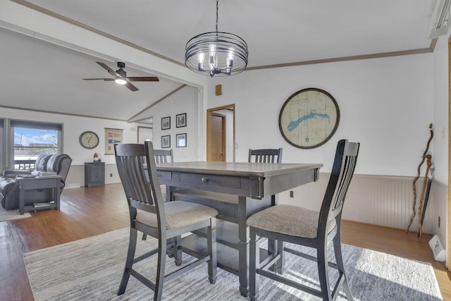 dining room with wood finished floors, a wainscoted wall, vaulted ceiling with beams, ornamental molding, and ceiling fan with notable chandelier