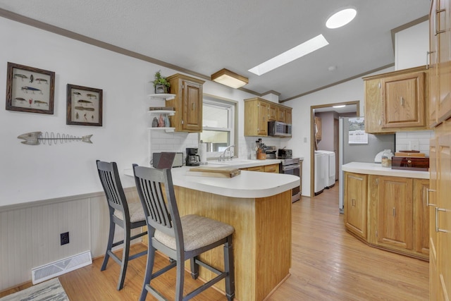 kitchen with visible vents, wainscoting, vaulted ceiling with skylight, appliances with stainless steel finishes, and a peninsula