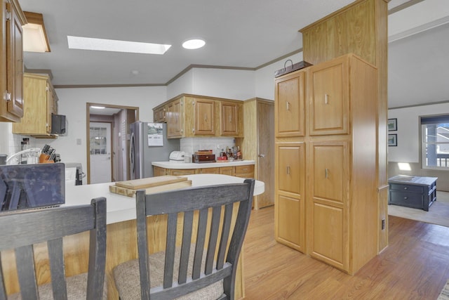 kitchen featuring light wood-type flooring, a skylight, freestanding refrigerator, light countertops, and tasteful backsplash