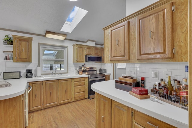 kitchen with light wood finished floors, a skylight, a sink, stainless steel appliances, and crown molding