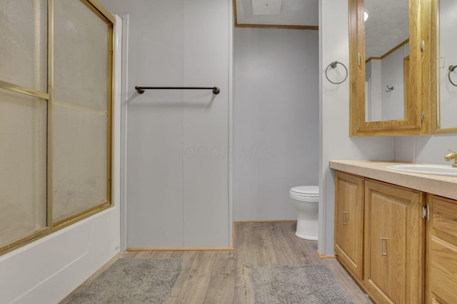 full bathroom with toilet, ornamental molding, wood finished floors, bath / shower combo with glass door, and vanity