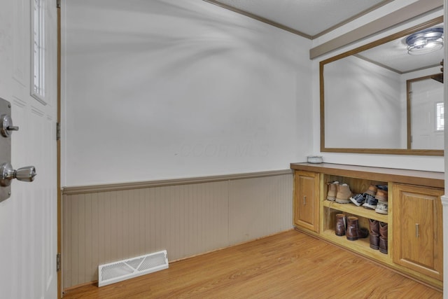 interior space featuring a wainscoted wall, crown molding, light wood-style flooring, and visible vents