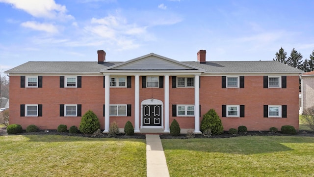 greek revival inspired property featuring a front lawn, a chimney, and a shingled roof
