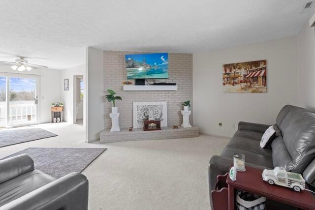 carpeted living area with a brick fireplace, a textured ceiling, and a ceiling fan