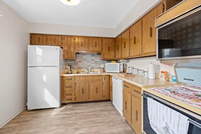 kitchen featuring a sink, white appliances, light wood finished floors, decorative backsplash, and light countertops