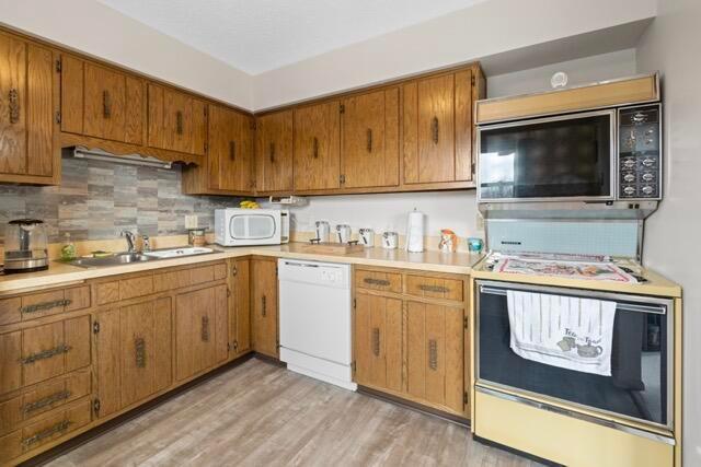 kitchen with light wood-style flooring, white appliances, light countertops, and a sink