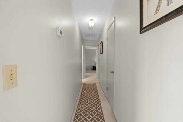 hall featuring visible vents, light colored carpet, and baseboards