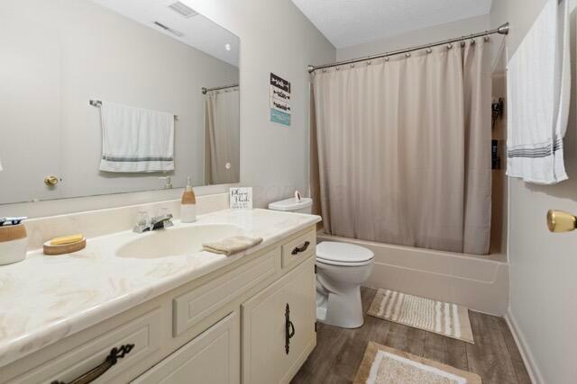 full bath with baseboards, toilet, wood finished floors, shower / bath combination with curtain, and vanity