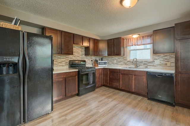 kitchen with light countertops, a sink, black appliances, and light wood-style floors