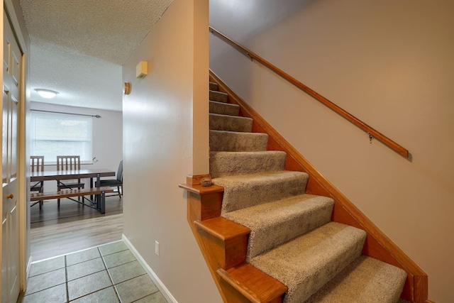 stairs featuring tile patterned flooring, a textured ceiling, and baseboards