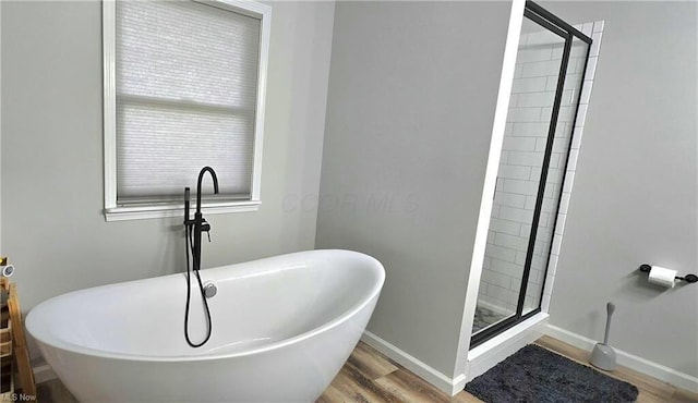 bathroom featuring a shower stall, wood finished floors, baseboards, and a freestanding tub