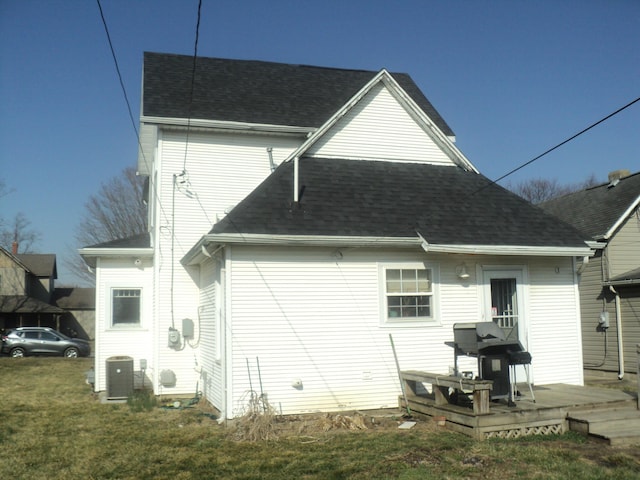 back of property with central AC unit, roof with shingles, and a lawn