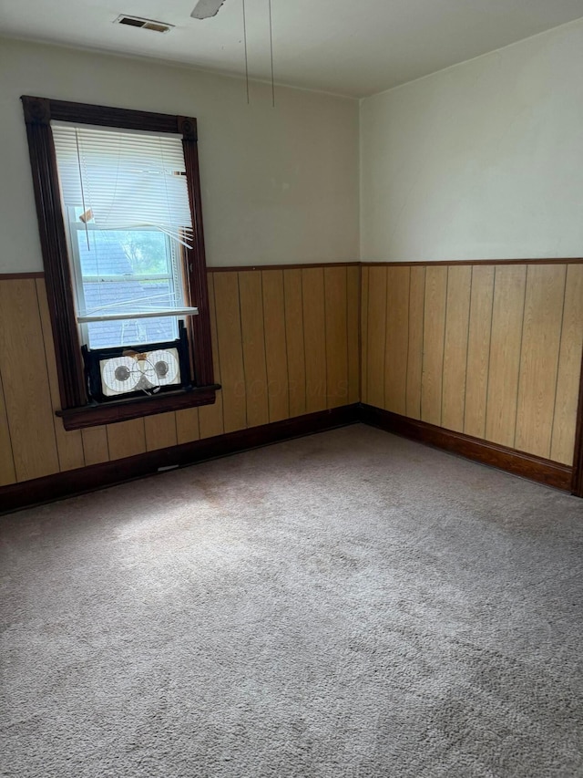 empty room featuring wooden walls, carpet, a wainscoted wall, and visible vents