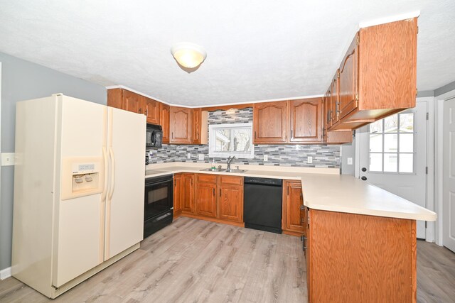kitchen featuring light countertops, a peninsula, a sink, black appliances, and brown cabinetry