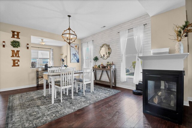 dining space featuring baseboards, a multi sided fireplace, wood finished floors, and a notable chandelier