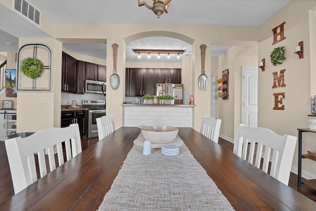 dining area with arched walkways, baseboards, visible vents, and wood finished floors