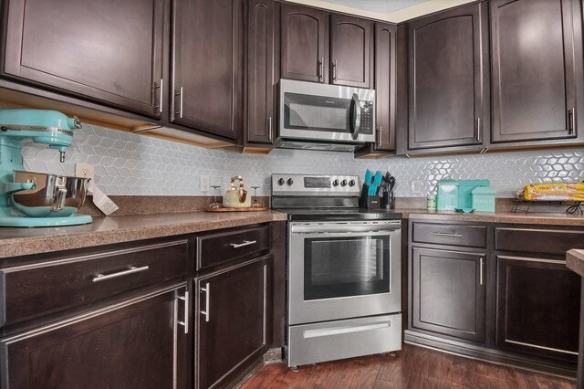 kitchen featuring dark brown cabinetry, backsplash, appliances with stainless steel finishes, dark countertops, and dark wood-type flooring